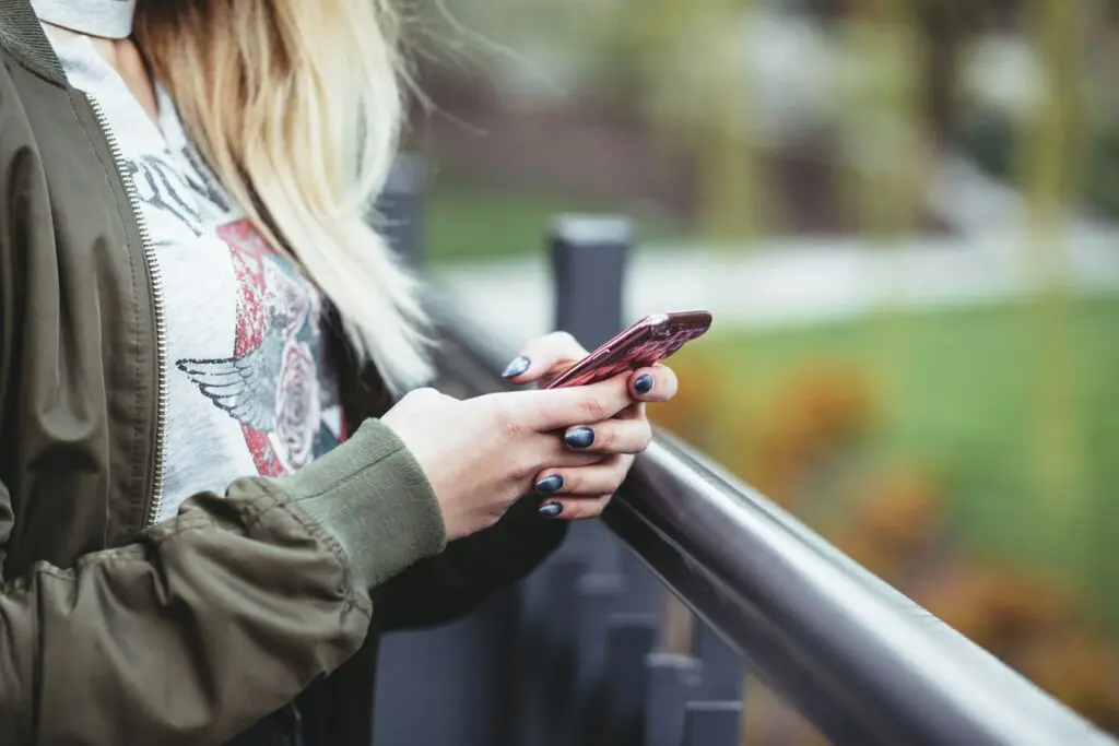 A woman standing outside by a railing with an iPhone in her hands