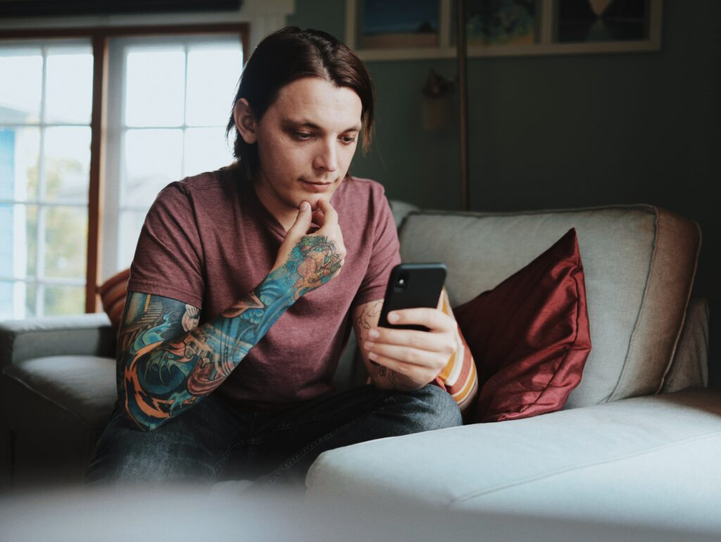 A photo of a young man with sleeve tattoos looking thoughtfully at his phone