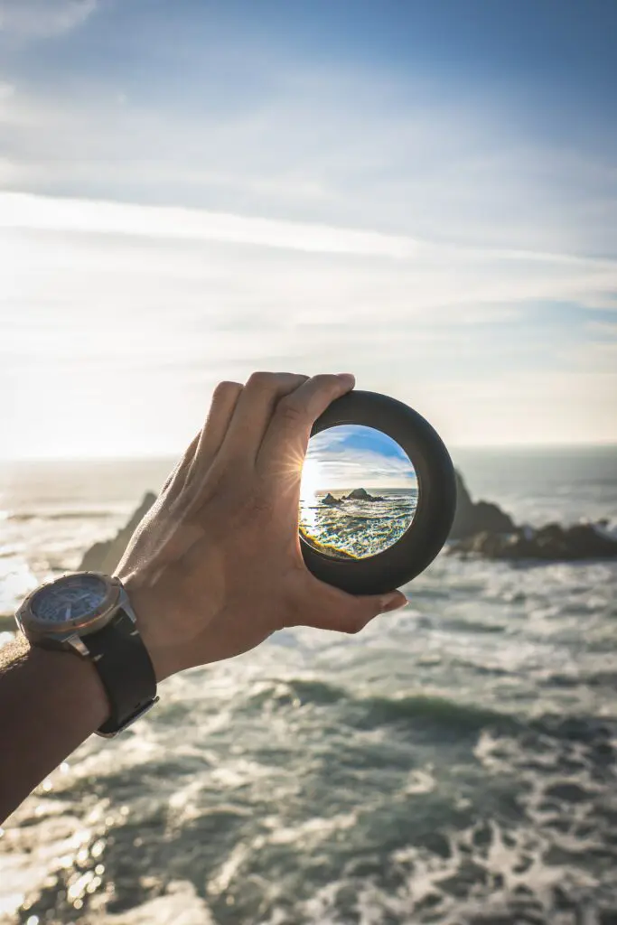 A hand holding a lens with a clear image of an ocean island in the center of the lens