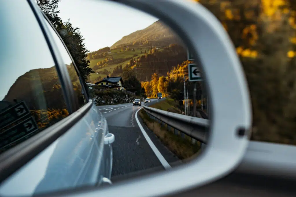 A photo taken in the side mirror of a vehicle, capturing the road, cars, and mountains in the rear