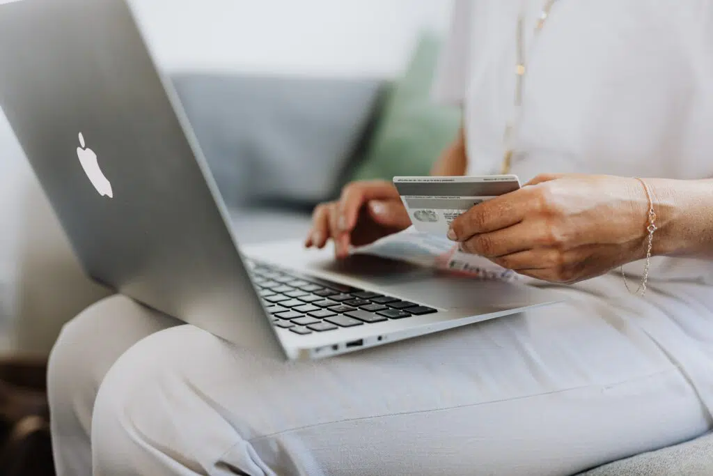 A woman sitting with a MacBook on her lap, holding a credit card in her hand